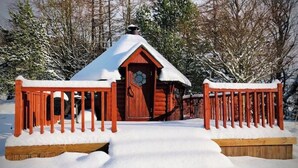 Une cabane en bois, dont le toit est recouvert de neige, et une clôture en bois devant.