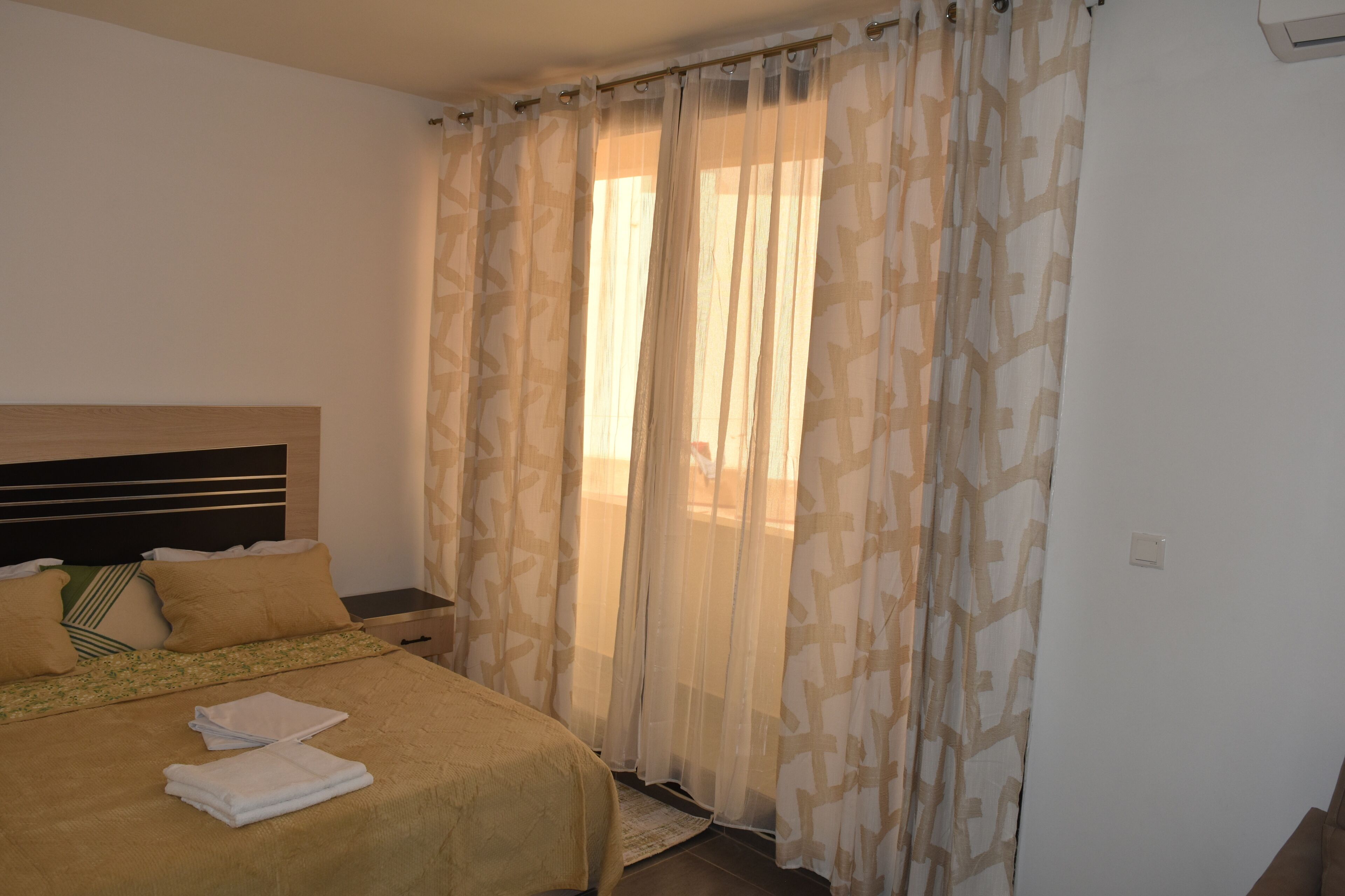 A hotel room with a bed, a nightstand, and sheer curtains.