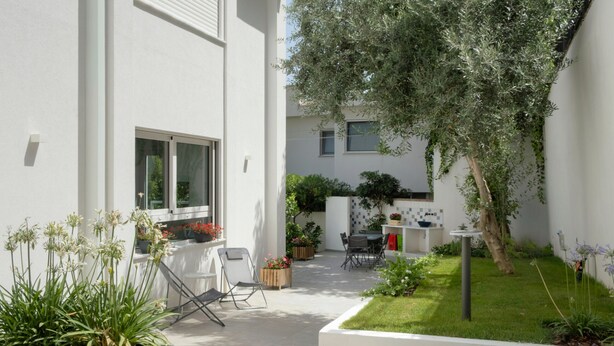 A modern outdoor patio with a dining area, a small garden, and a white building with a window and a door. - Addaura Marina Apartment by Wonderful Italy (Palermo)