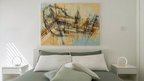 A modern bedroom with a large bed, two bedside tables, a wall-mounted light, and a painting. - Addaura Marina Apartment by Wonderful Italy (Palermo)