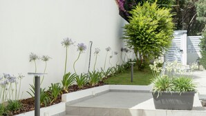A modern outdoor garden with a white wall, a small seating area, and a variety of plants and flowers. - Addaura Marina Apartment by Wonderful Italy (Palermo)