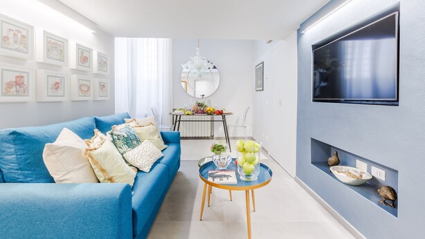 Un salón moderno con un sofá azul, una mesa de centro y un televisor montado en la pared.