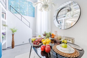 A dining area with a glass table, fruit, and a mirror on the wall. - The Atelier House Lucca (Lucca)