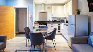 A modern kitchen with white cabinets, a refrigerator, and a dining area with a glass table and chairs. - Spacious Ensuite 2-Bedroom Flat in Kelham Island (South Yorkshire)