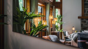 A cozy room with a large mirror, wooden walls, and a stone fireplace. There are potted plants and hanging lamps. - Designer Forest Cabin w/Hot Tub Near CherrySprings (Coudersport)