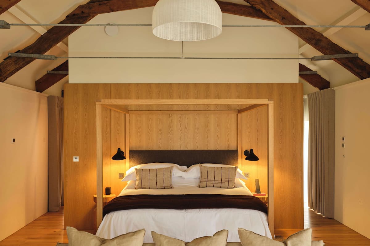 Ein Schlafzimmer mit einem Holzkopfteil, einem großen Bett mit weißer Bettwäsche, zwei Nachttischlampen und einer Pendelleuchte.