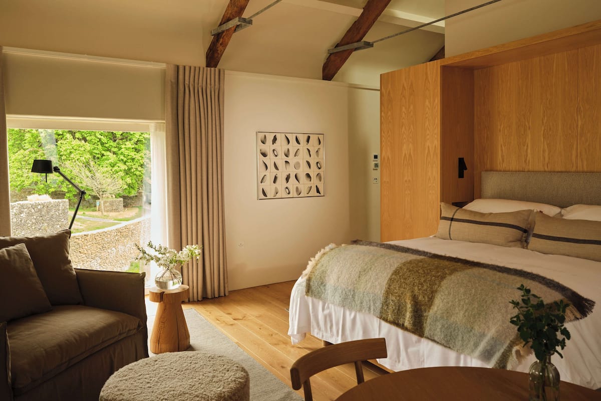Ein Schlafzimmer mit Bett, Schreibtisch, Stuhl, Sofa, einem Fenster mit Vorhängen und einem Wandbild.