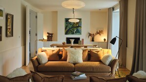 A modern living room with a brown sofa, a dining table, and a large painting on the wall. - Fowlescombe Farm (Ivybridge)
