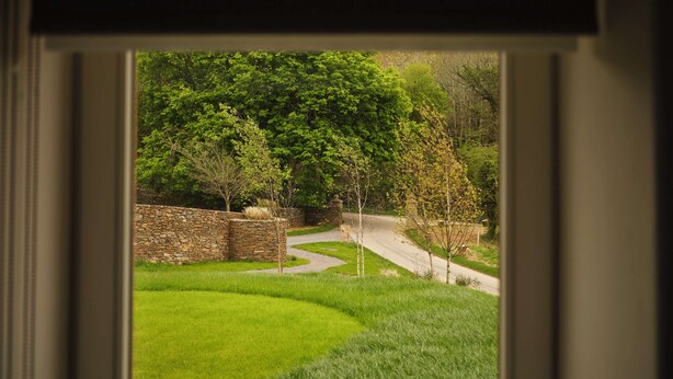 A view through a window of a stone wall, a curved driveway, and lush green grass. - Fowlescombe Farm (Ivybridge)
