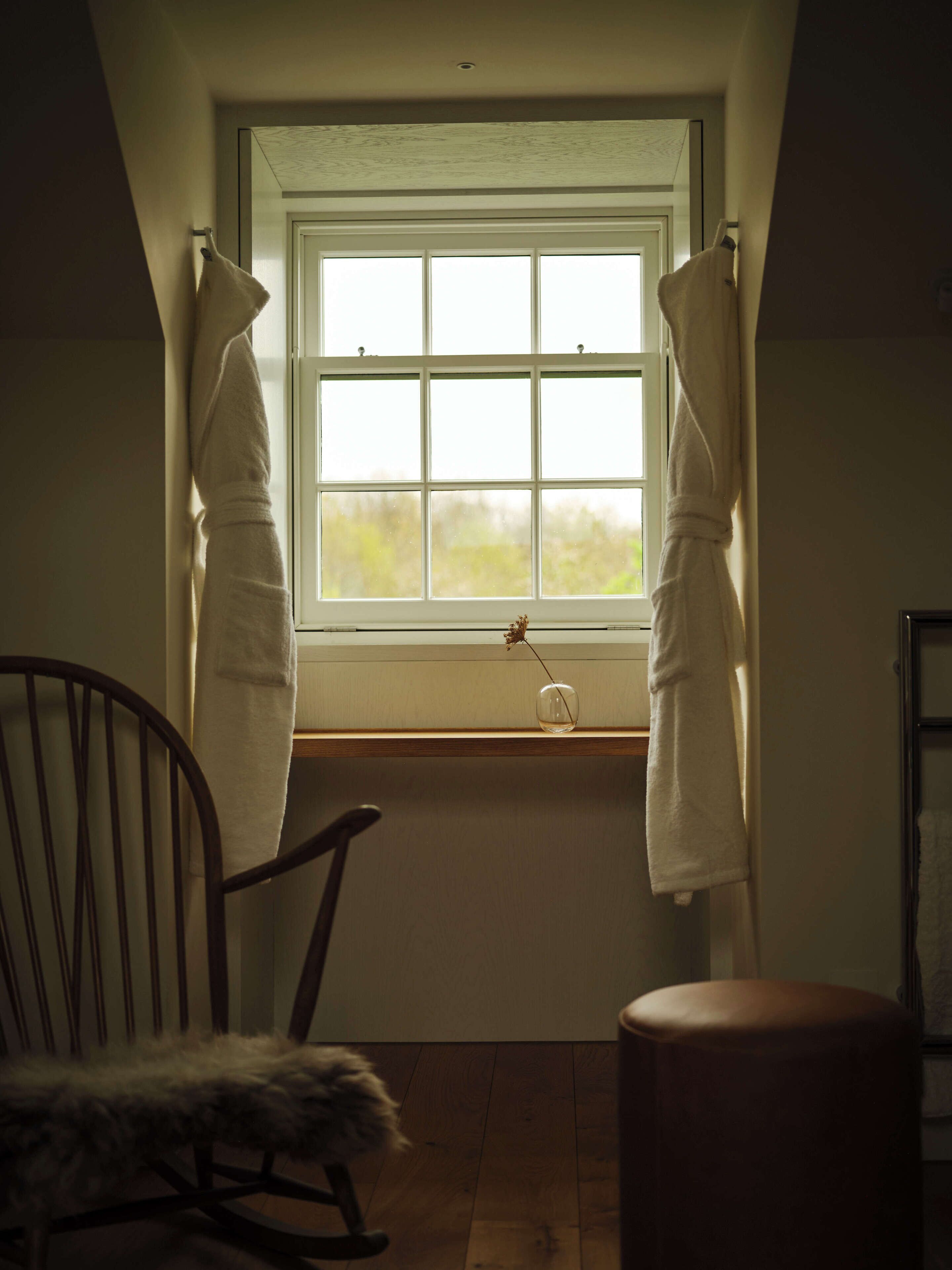 Una habitación con ventana, una silla y un taburete pequeño.