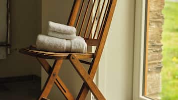 A wooden chair with towels placed on it, positioned near a window with a view of greenery outside.