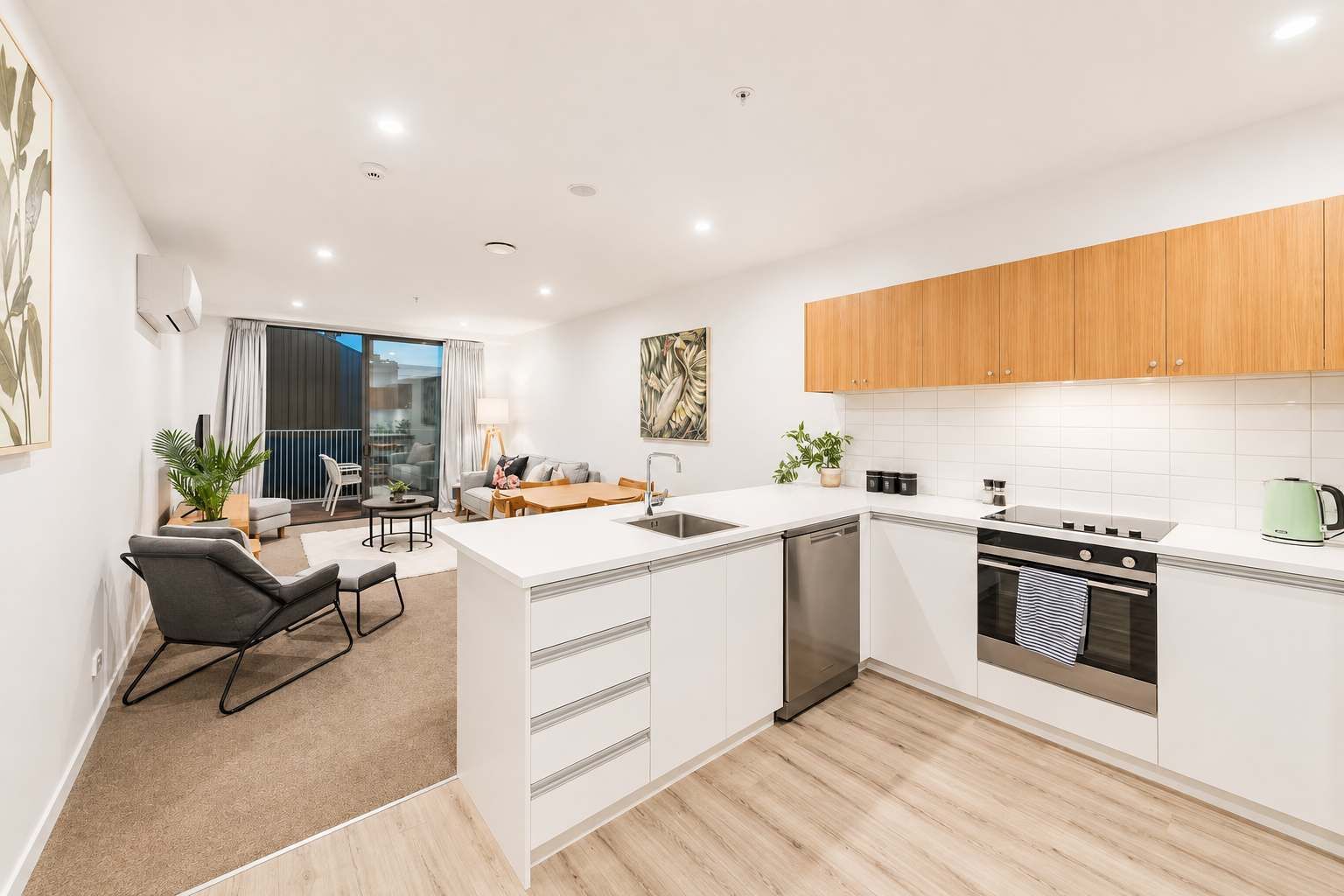 A modern kitchen with white cabinetry, a central island, and a dining area with a sofa and table.