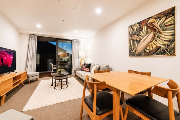 A modern living room with a flat-screen TV, a dining table, and a sofa.