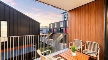 A balcony with a wooden table and chairs, a potted plant, and a view of adjacent buildings.