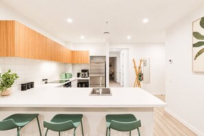 Una cocina moderna con una isla central, electrodomésticos de acero inoxidable y taburetes de bar verdes.