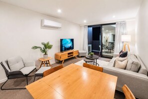 Una sala de estar moderna con una mesa de comedor de madera, sofás, un televisor y un balcón con cortinas.