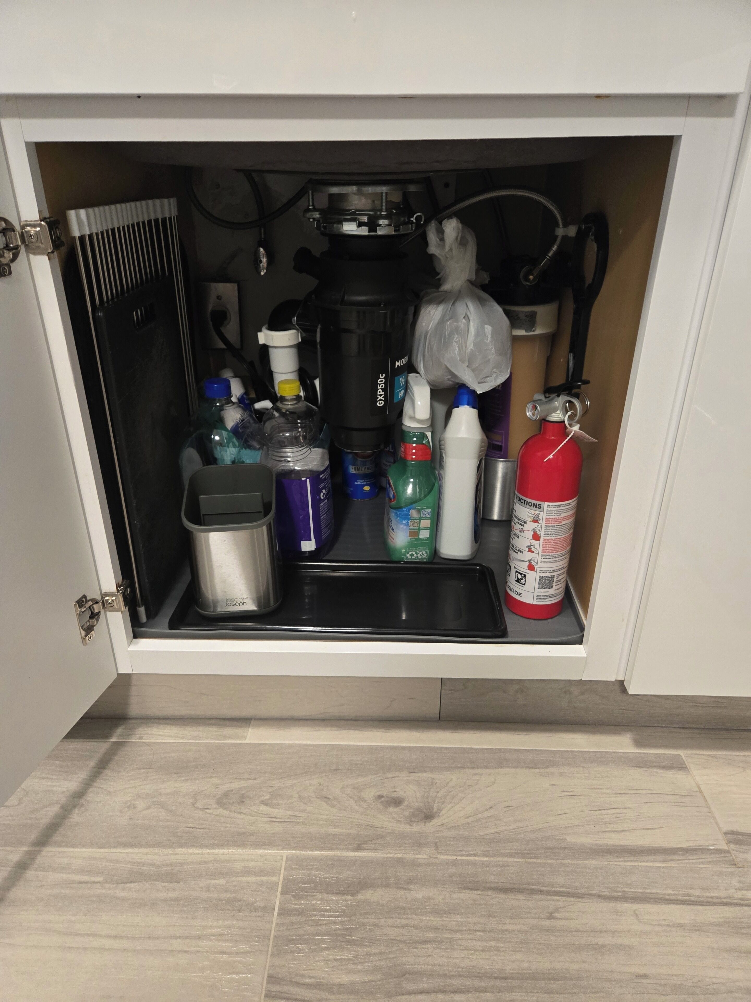 Un armario de cocina con varios objetos, incluyendo una cafetera, botellas, un extintor y un cubo de basura.