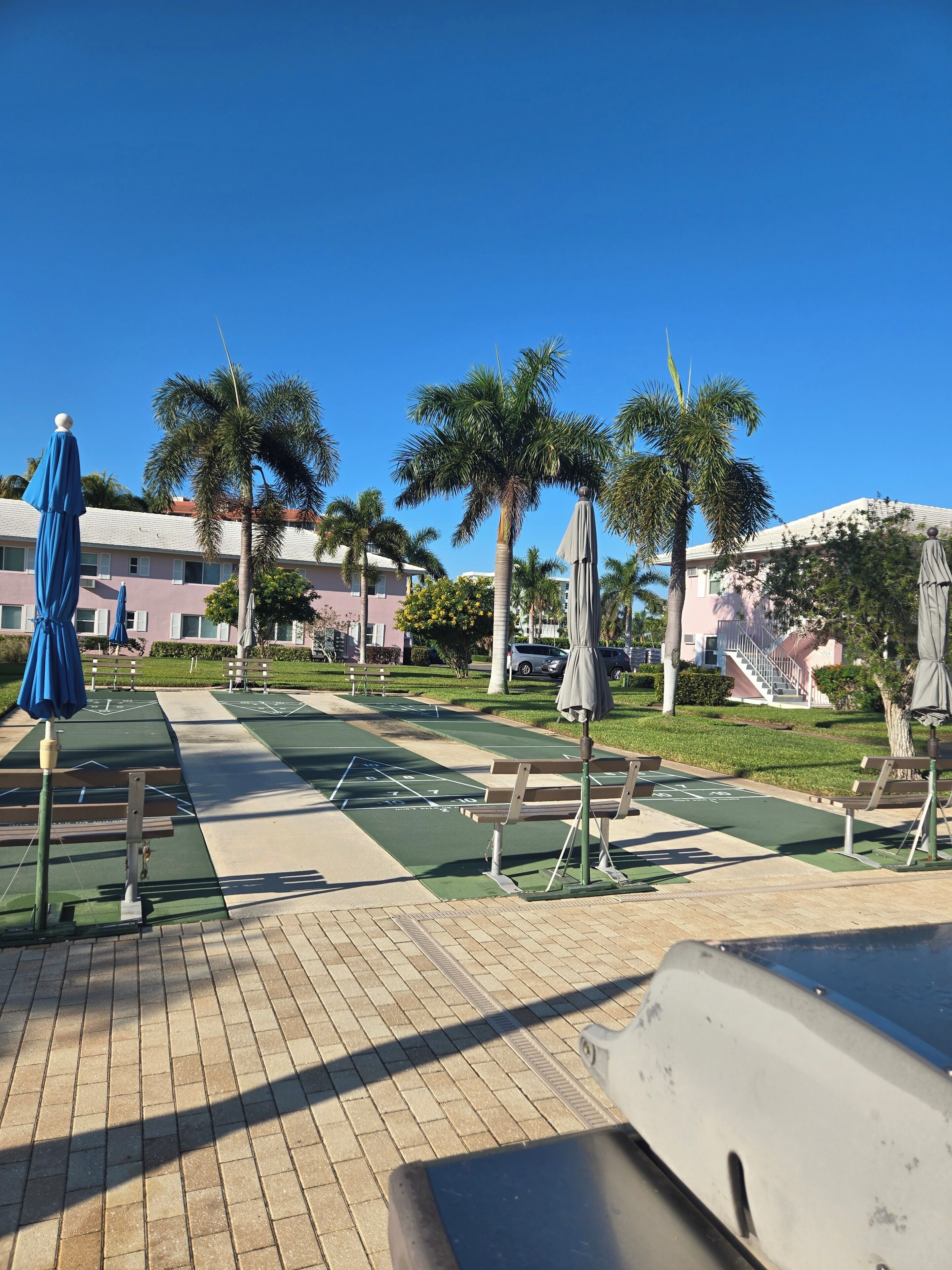Un espacio al aire libre soleado con una cancha de juego de hoquey, bancos y sombrillas.