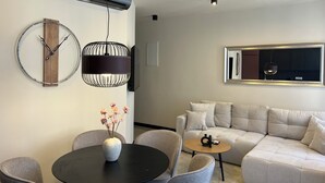A modern living room with a round dining table, grey upholstered chairs, a beige sofa, a black pendant light, and a mounted TV. - Luxury apartman Central 1, Crikvenica (Crikvenica)
