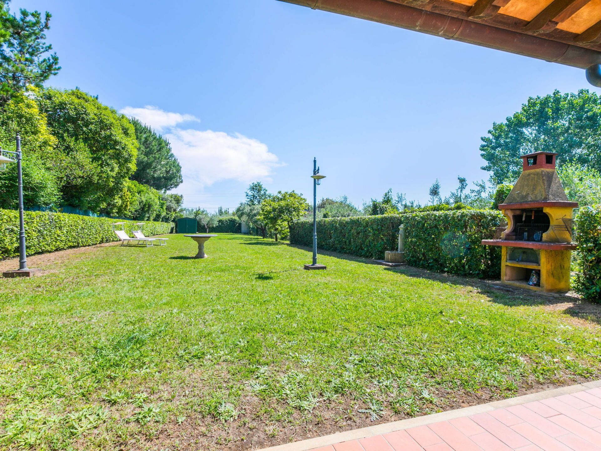 Ein gepflegter Garten mit Stehbank, einer Pergola und einer kleinen Außenküche.