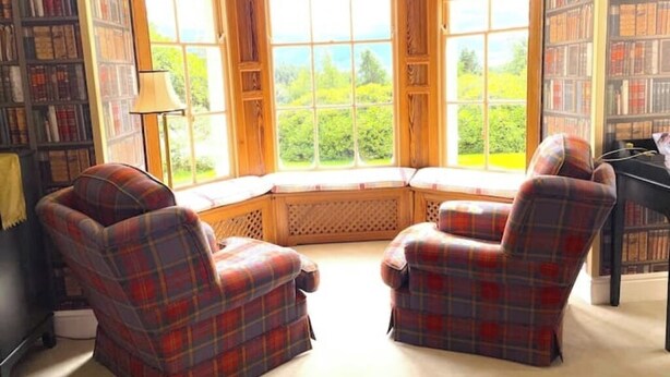 A corner seating area with a view of greenery through large windows, flanked by bookshelves. - The Squirrel Room Energetic & Inspiring (Kinross)