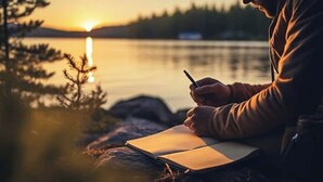 A person sitting by a lake at sunset, writing in a notebook. - The Squirrel Room Energetic & Inspiring (Kinross)