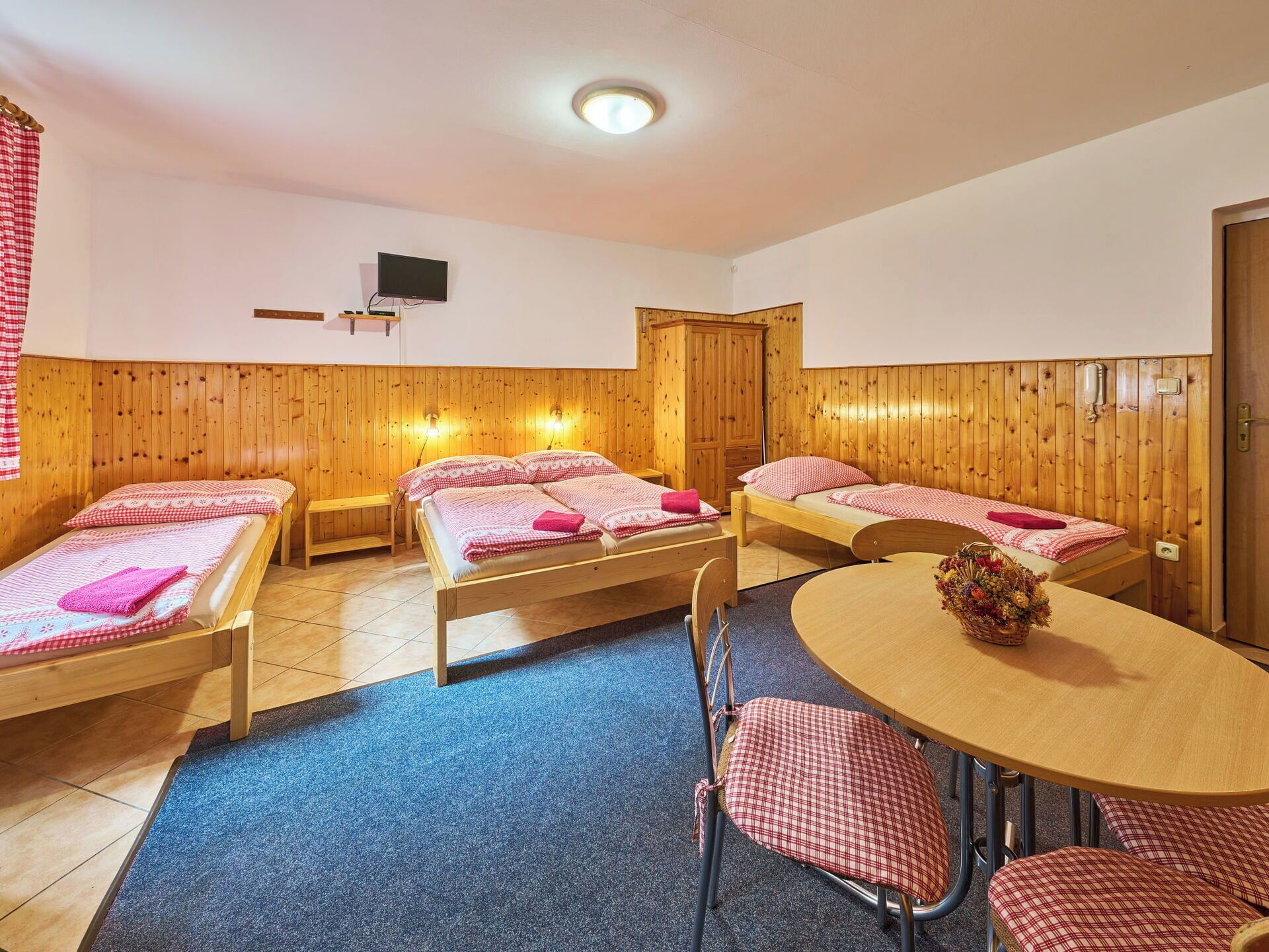 A room with three wooden beds, a TV, a wooden wardrobe, and a round table with chairs.