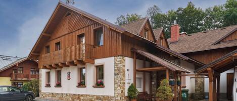 A wooden chalet with a stone facade, a covered porch, and a gravel driveway.