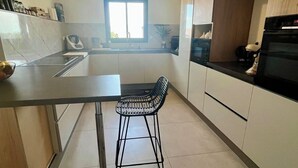 A modern kitchen with a central island, a window, and a built-in oven. - Villa panoramic view (Narbonne)