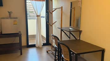 Una habitación pequeña con escritorio, silla y espejo. Tiene una puerta corredera con cortina, una planta en maceta y un letrero en la pared.