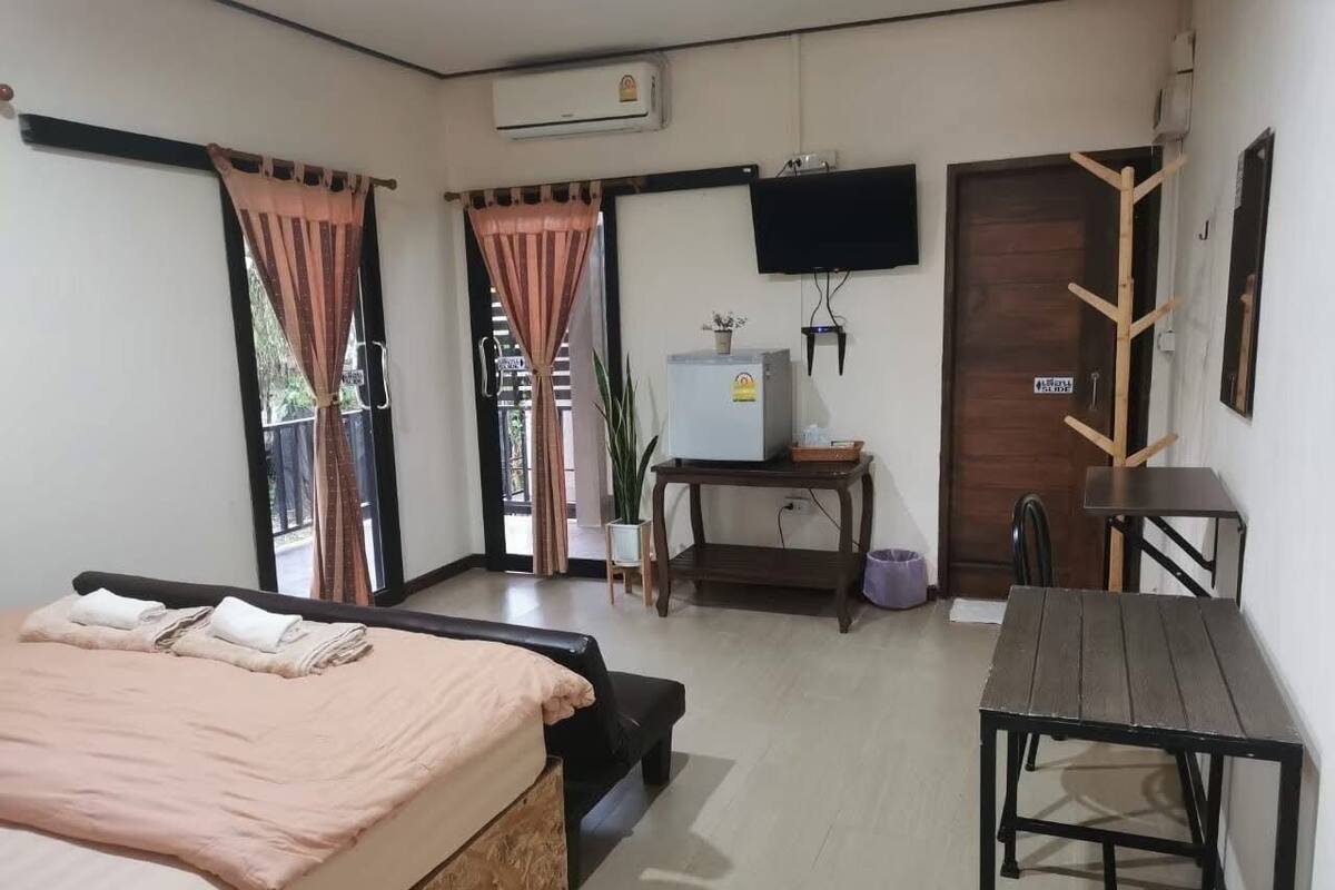 A bedroom with a bed, a desk, a chair, a TV, and a door.