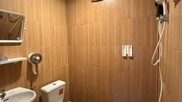 Een kleine, compacte badkamer met houten lambrisering, een toilet, een wastafel en een douchehoek.
