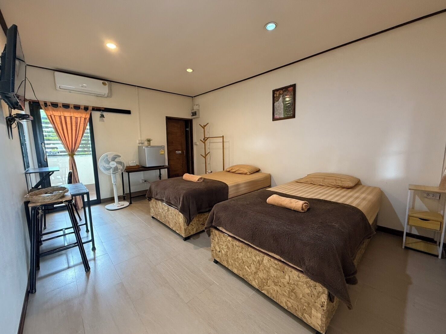 A room with two beds, a desk, a chair, a fan, and a small table.