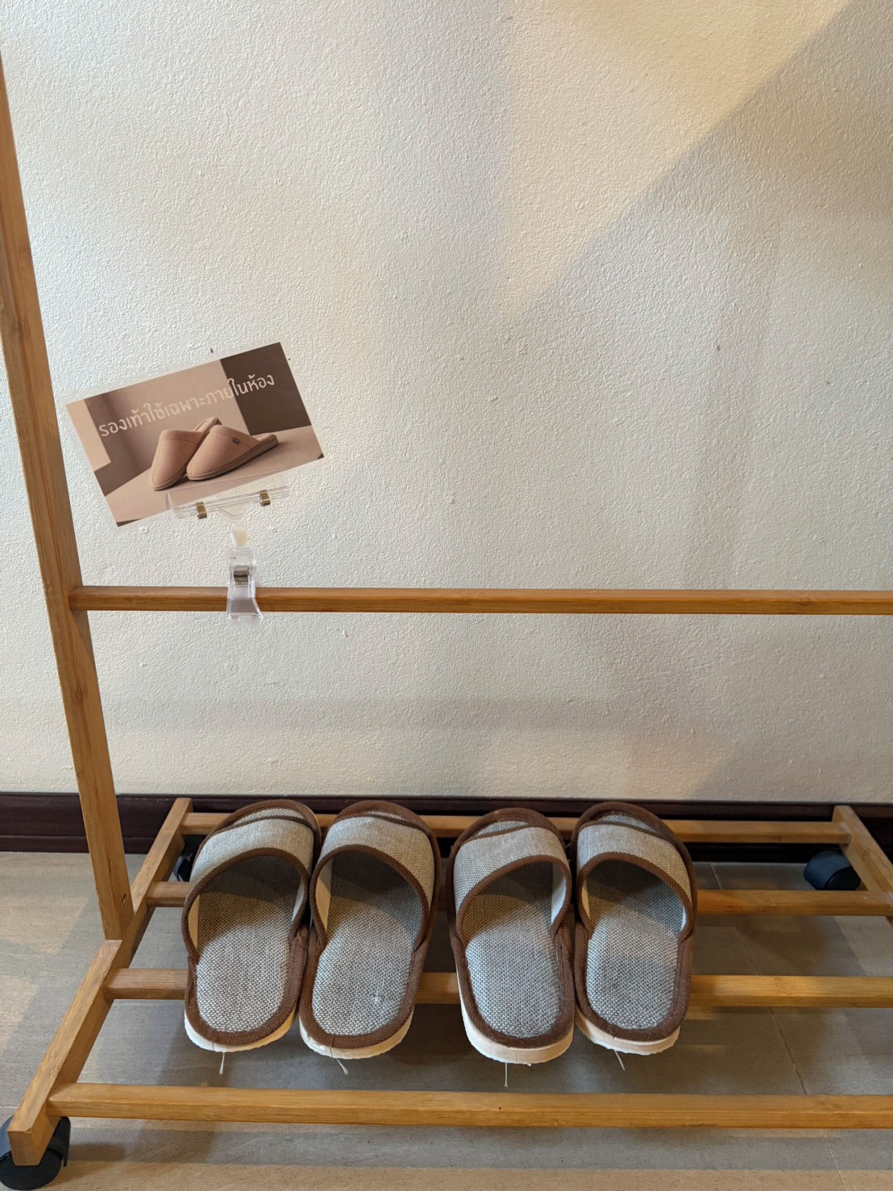 A wooden shoe rack with four pairs of slippers, a wall-mounted advertisement, and a wooden floor.