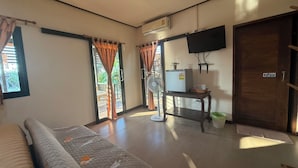 A room with a bed, a table with a fan, a TV, and a door. - Hug Wang Homestay (Wang Saphung)
