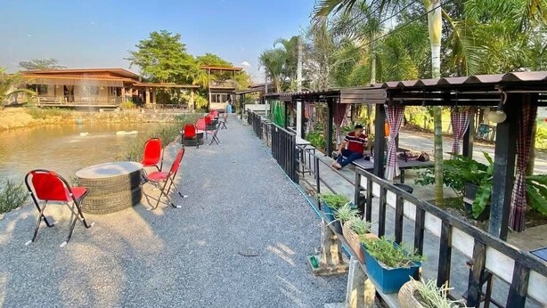 A riverside restaurant with outdoor seating, a view of the river, and a covered area with plants. - Hug Wang Homestay (Wang Saphung)