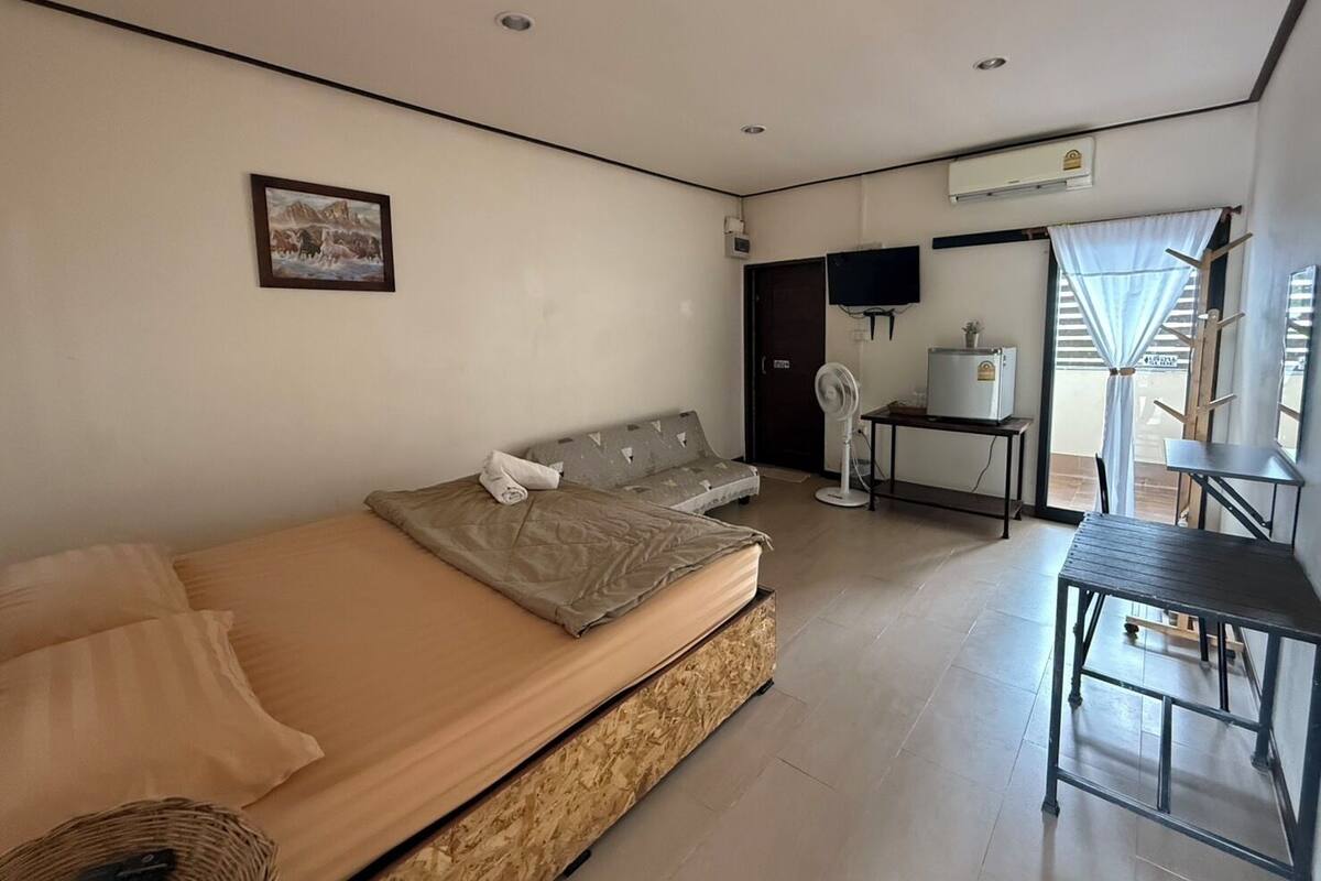 A bedroom with a bed, a small table, a fan, and a TV.