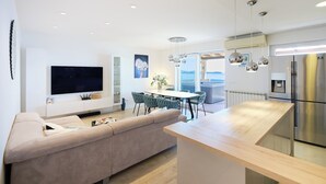 A modern kitchen with a central island, a dining area with green chairs, and a large flat-screen TV mounted on the wall. - Hedera Estate, Hedera A54 (Zupa dubrovacka)