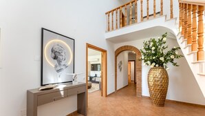 Un intérieur moderne avec un escalier, un grand vase rempli de fleurs et une œuvre d’art encadrée accrochée au mur.