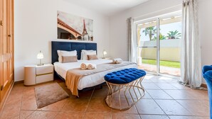 Une chambre à coucher comprenant un lit, des tables de chevet, un pouf bleu, un tableau représentant la Tour Eiffel et une porte-fenêtre coulissante donnant sur un balcon.