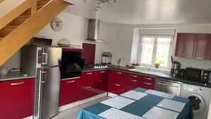 Een moderne keuken met rode kastjes, roestvrijstalen apparatuur, een inbouwoven en een tafel gedekt met witte placemats.