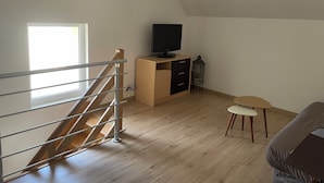 Een kamer met een houten trap, een bureau met een televisie, een klein tafeltje en een lantaarn.