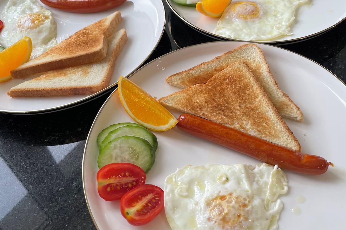 A breakfast setup with plates of toast, sausages, eggs, and fruit.