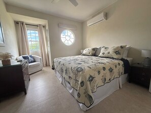 A bedroom with a bed, a chair, a dresser, a window, and an air conditioning unit. - Jack's Place - by ZenBreak (Mullins)