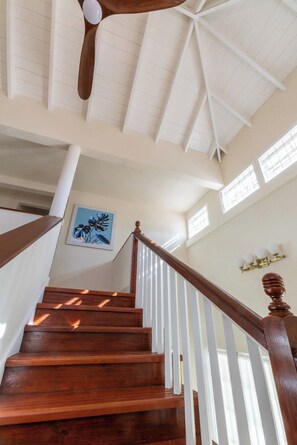 A wooden staircase with white railings leading to a high ceiling with a fan. - Jack's Place - by ZenBreak (Mullins)