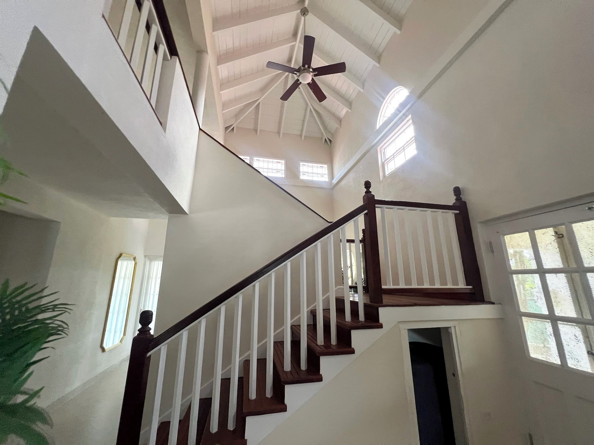 Un intérieur à plusieurs niveaux, doté d’un escalier central, d’un ventilateur de plafond et de fenêtres laissant entrer la lumière naturelle.