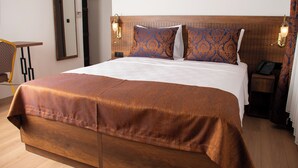 Une chambre d’hôtel avec un grand lit, une tête de lit en bois, deux coussins à motifs, une table de chevet avec une lampe et un téléphone.