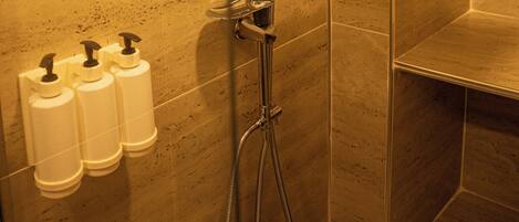 A shower area with a handheld showerhead and a wall-mounted showerhead, a towel rack, and three bottles of shampoo.