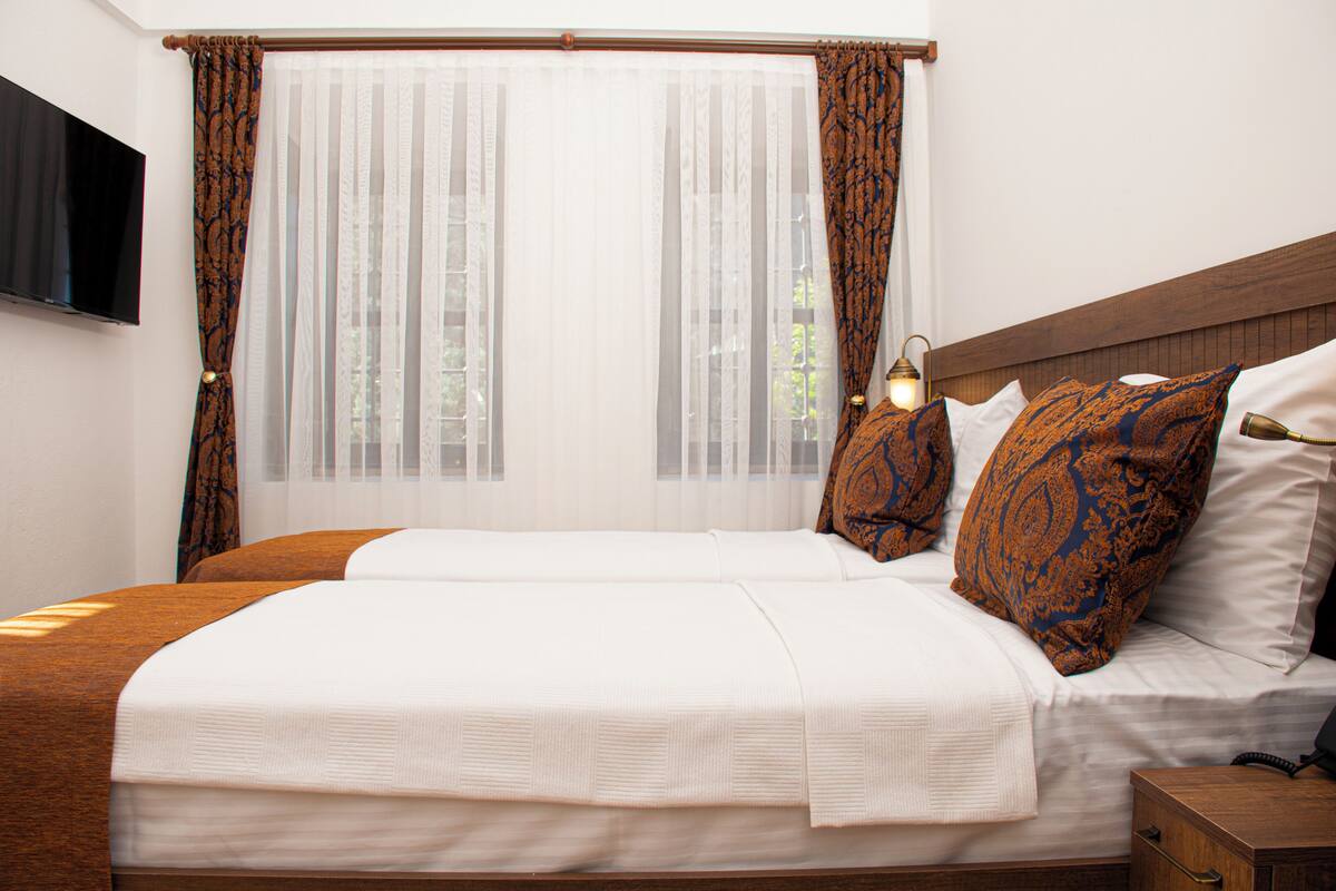 A double bed with white linens, two patterned pillows, a bedside table with a lamp, and a TV mounted on the wall.