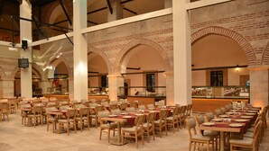 Un vaste espace dédié à la salle à manger, avec de nombreuses tables et chaises, de hauts plafonds ornés d’arcs en briques et un comptoir central.